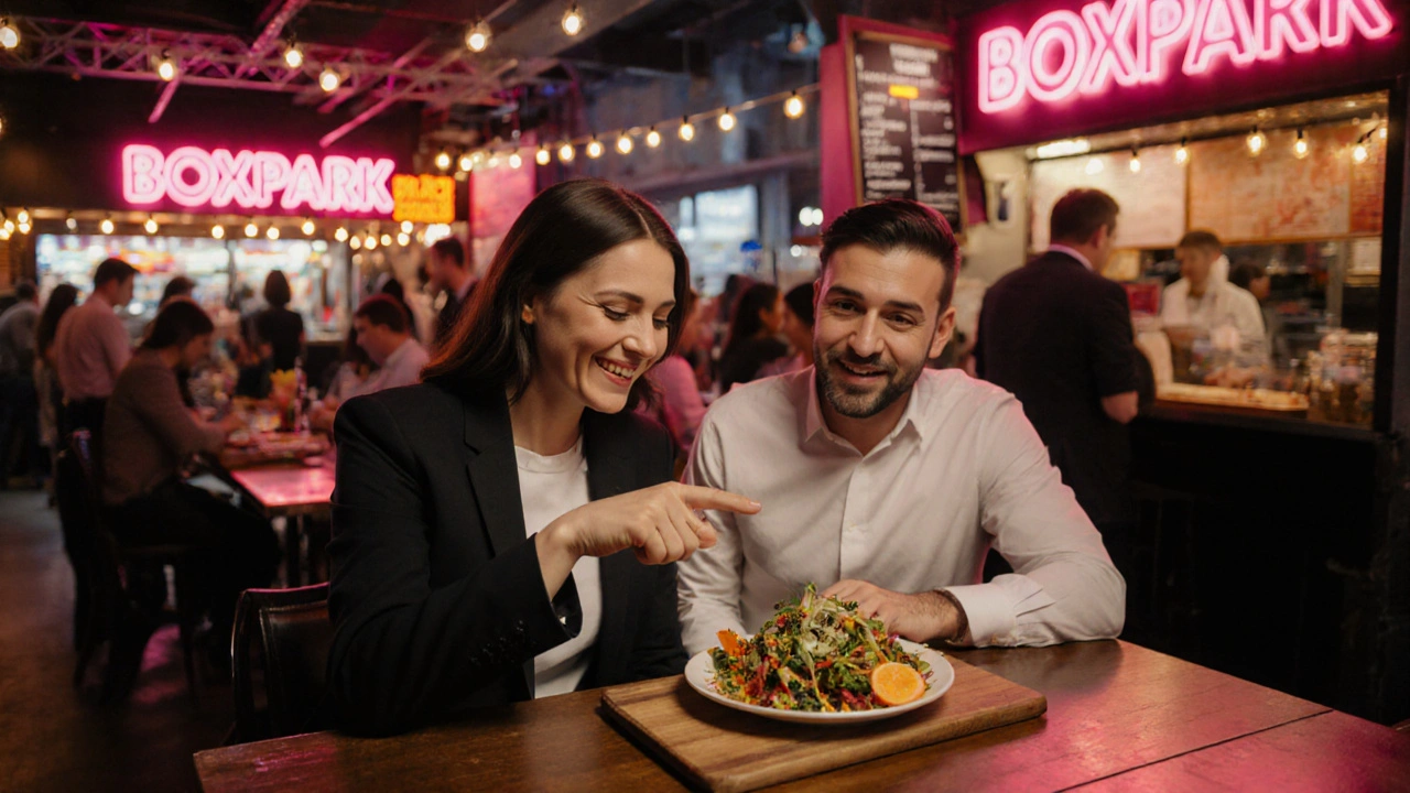 Escort and client sharing a vegan meal at Boxpark Croydon with neon lights.
