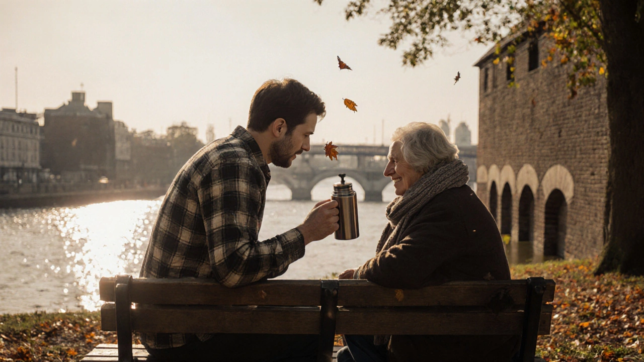 Male companion offering tea from a thermos to an elderly woman on a garden bench at Royal Arsenal Riverside, autumn leaves drifting nearby.